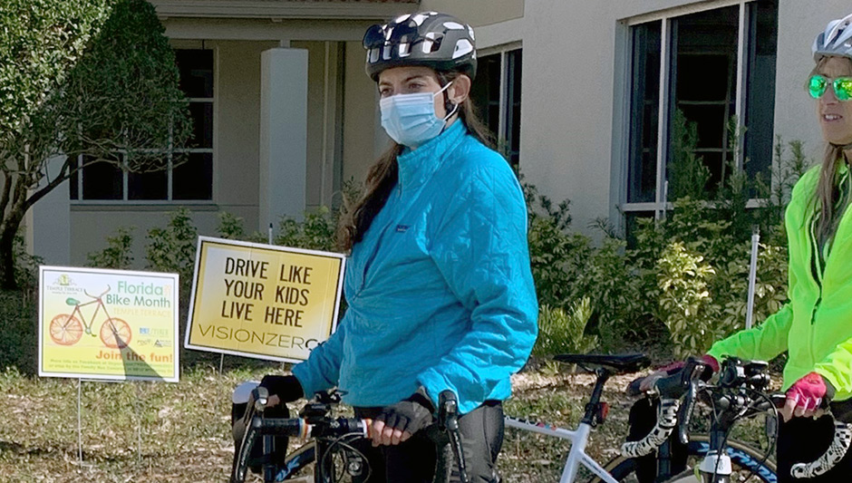 people standing next to their bicycles with "drive like your kids live here" signs in the background